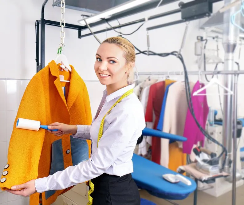 Woman holding a yellow coat with a cleaning tool in a dry cleaning setting